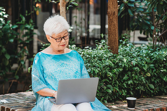 Weißhaarige Frau mit Brille arbeitet mit Laptop im Freien