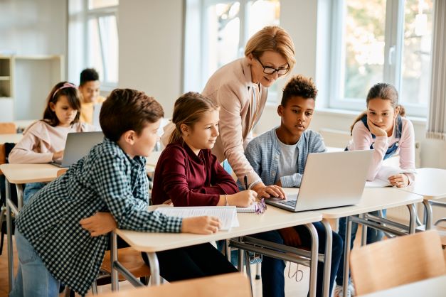 Lehrerin mit SchülerInnen (ca. 12 Jahre alt) vor einem Computer im Klassenzimmer